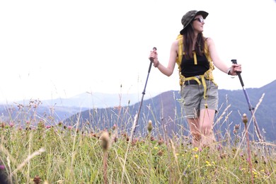 Young hiker with backpack and trekking poles in mountains, space for text