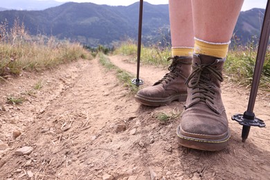 Young hiker with trekking poles in mountains, closeup. Space for text