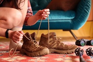 Young woman tying her trekking shoes indoors, closeup