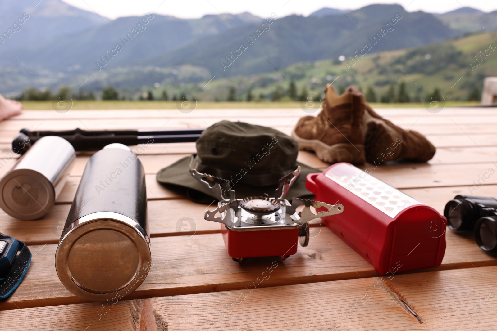 Photo of Different hiking equipment and tools at wooden table near mountains, closeup