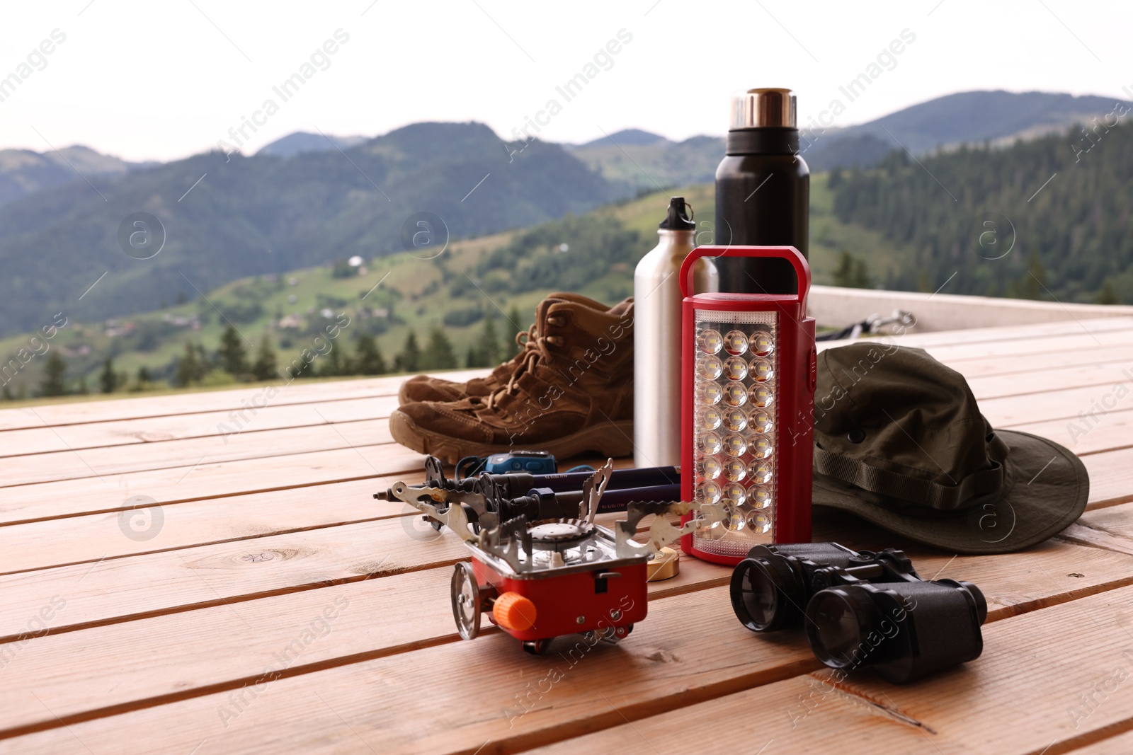 Photo of Different hiking equipment and tools at wooden table near mountains, space for text