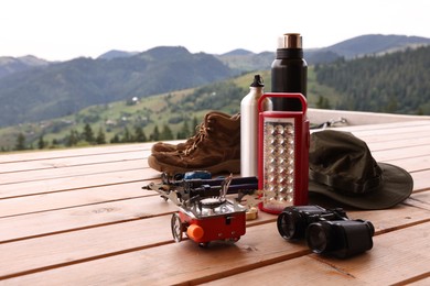 Photo of Different hiking equipment and tools at wooden table near mountains, space for text