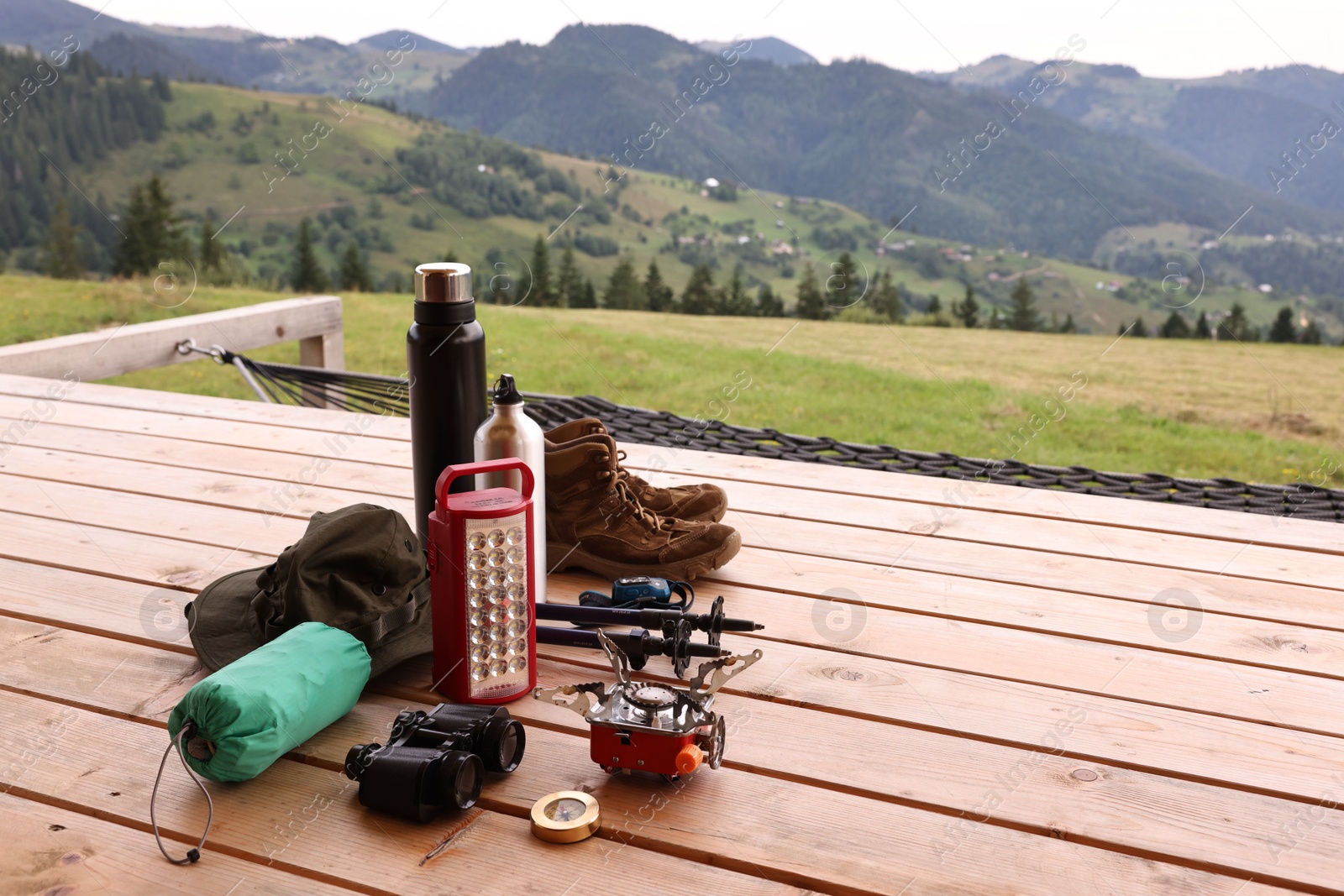 Photo of Different hiking equipment and tools at wooden table near mountains, space for text