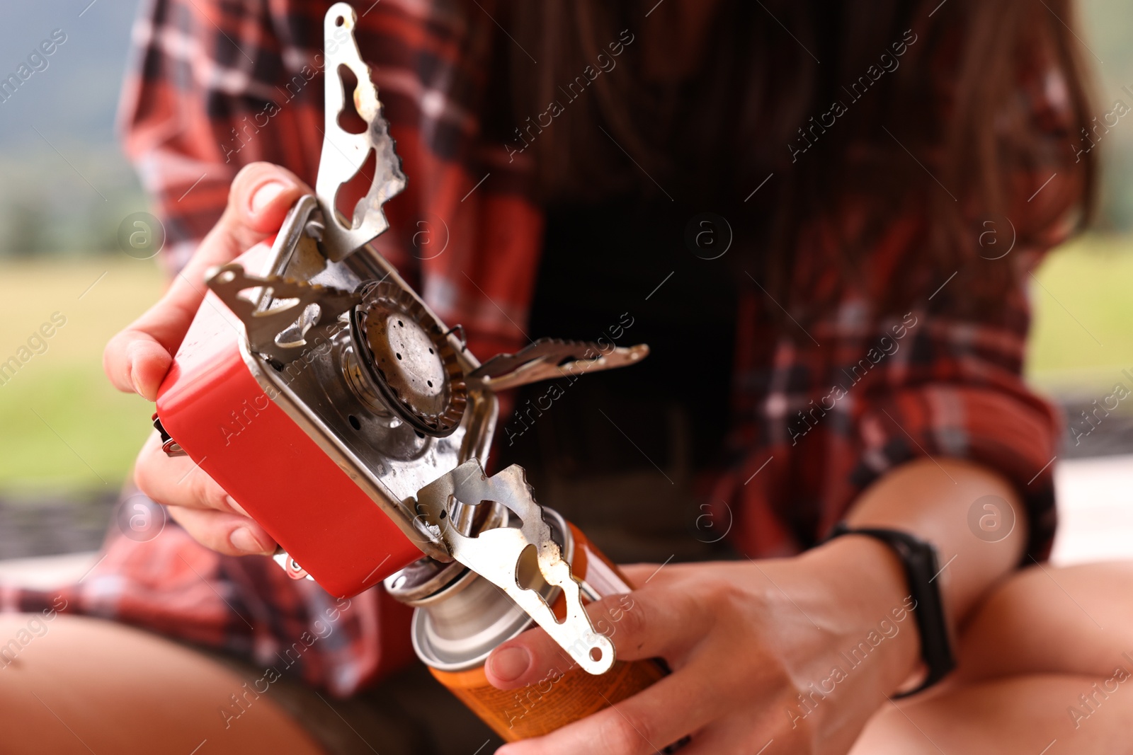 Photo of Young woman with camping stove and bottled gas outdoors, closeup