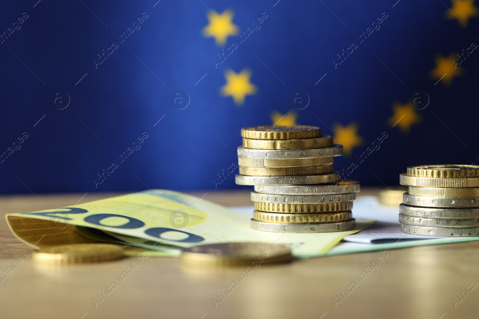 Photo of Euro banknotes and coins on table against European Union flag, closeup