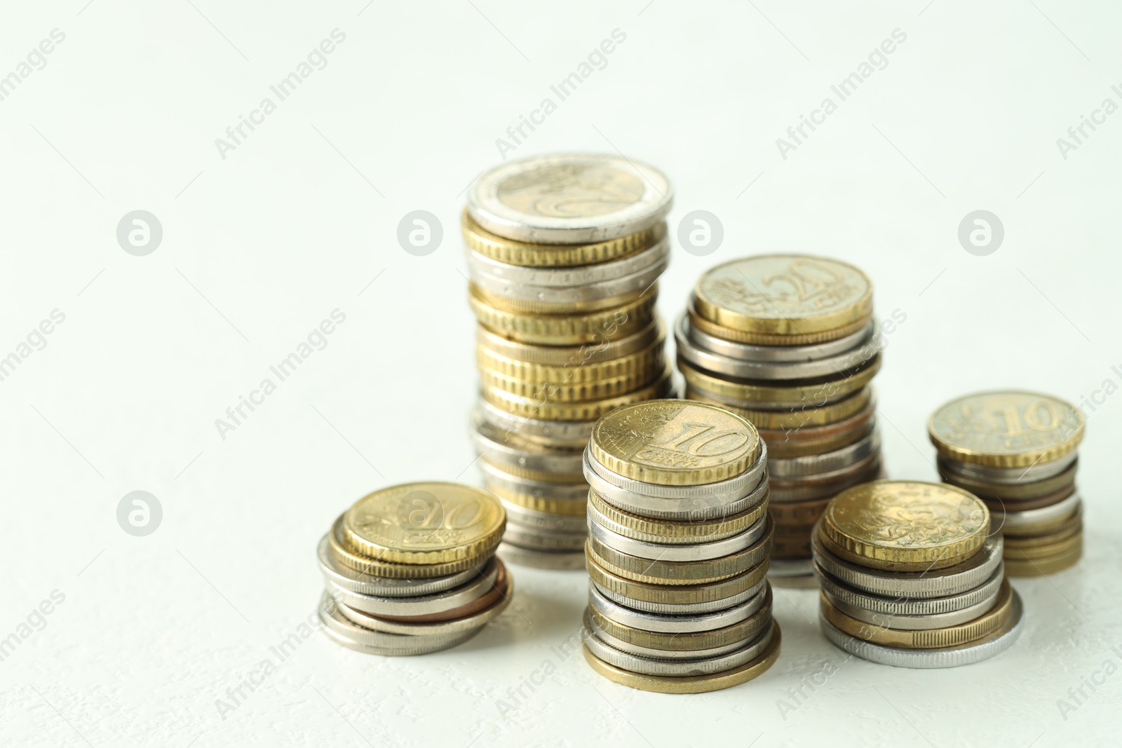 Photo of Stacks of euro coins on white textured table, closeup