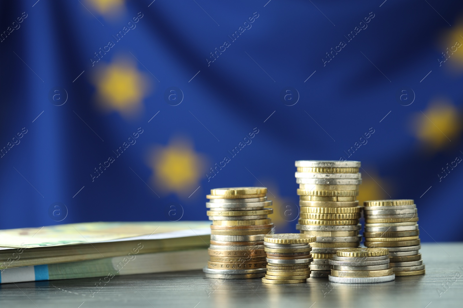 Photo of Stacks of coins and euro banknotes on grey table, closeup