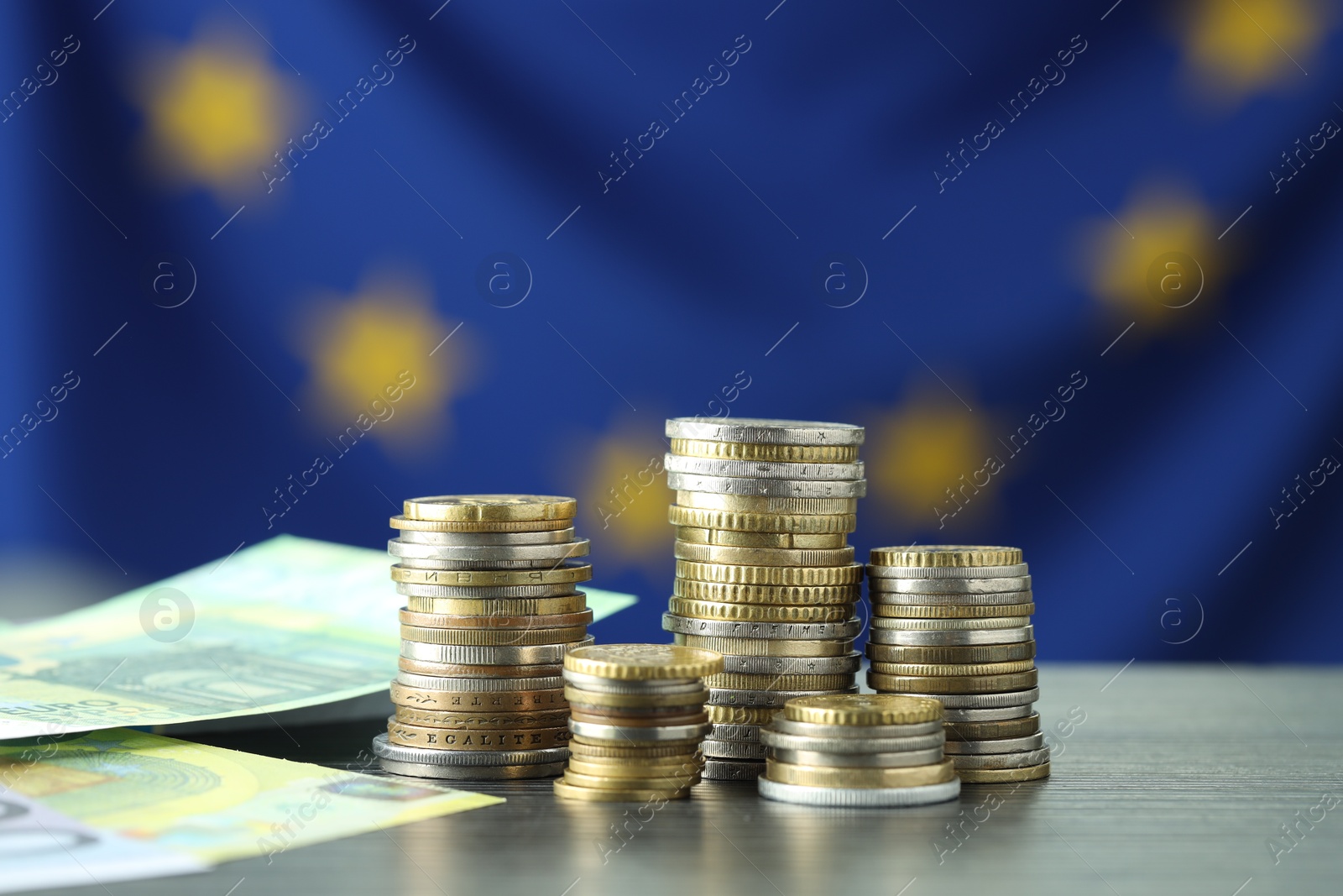 Photo of Stacks of coins and euro banknotes on grey table, closeup