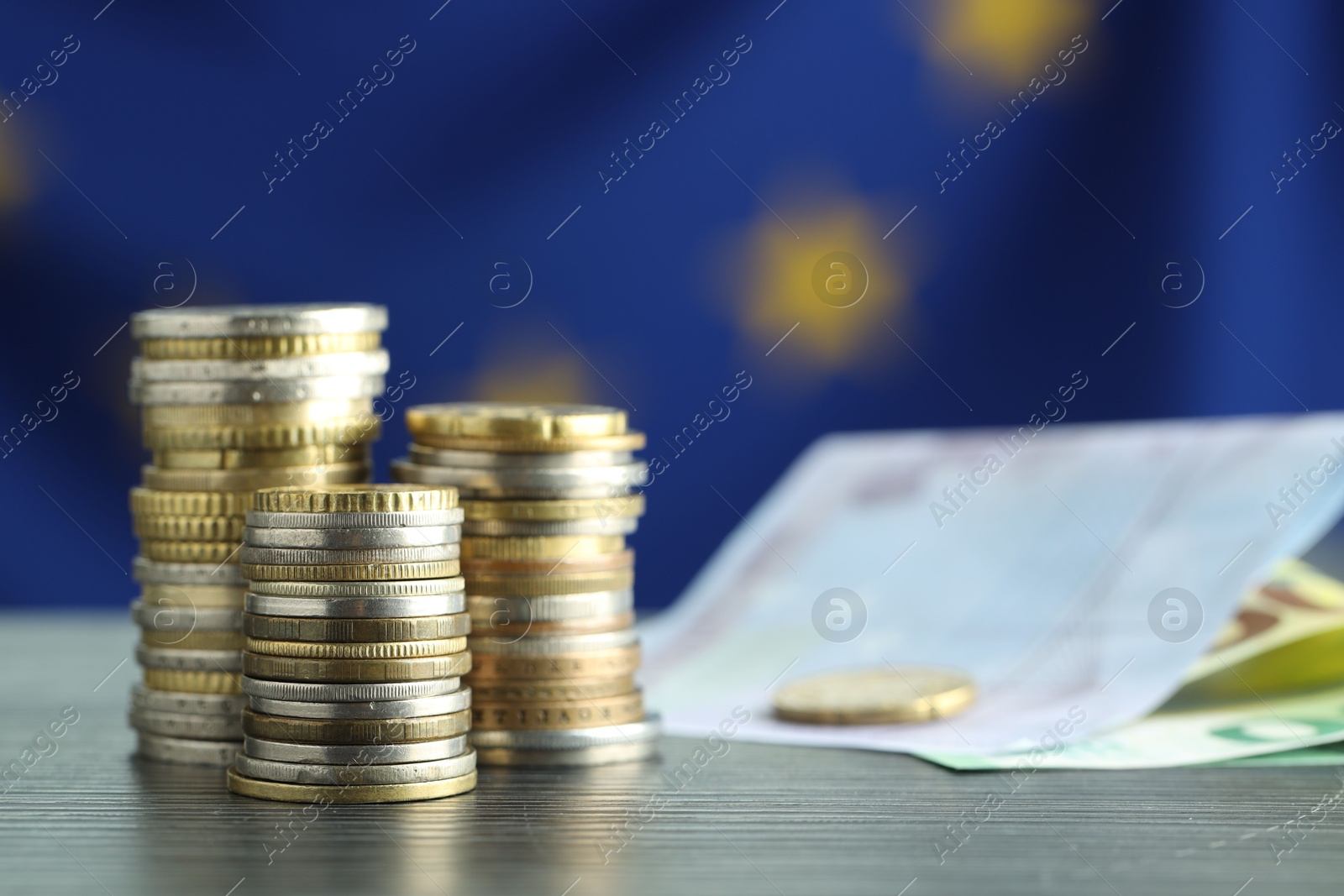 Photo of Stacks of coins and euro banknotes on grey textured table, closeup