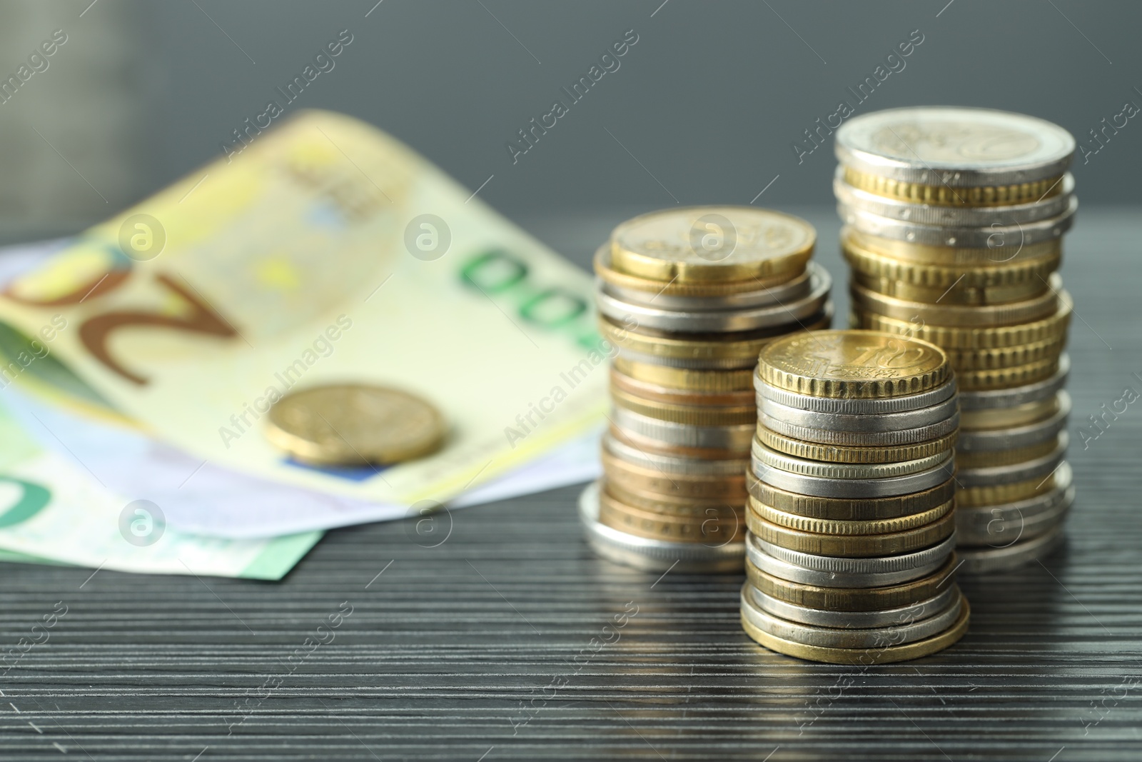 Photo of Stacks of coins and euro banknotes on grey textured table, closeup