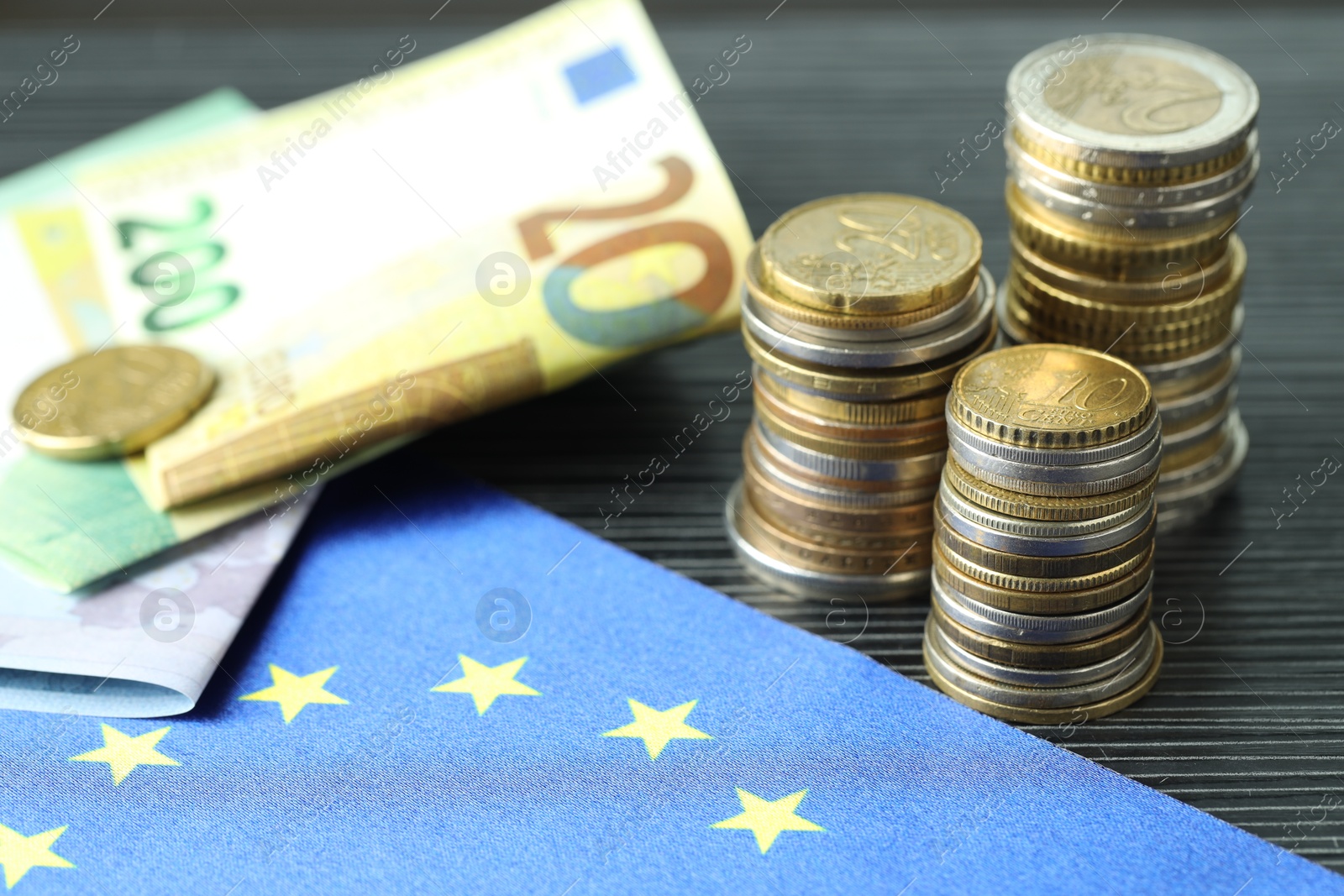 Photo of Stacks of coins, euro banknotes and European Union flag on grey textured table, closeup