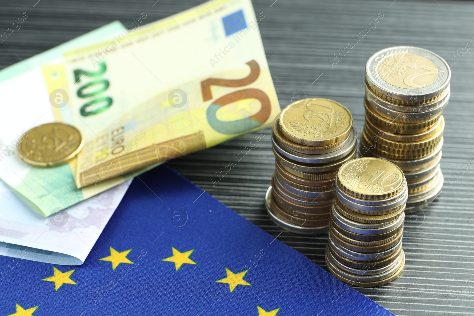 Photo of Stacks of coins, euro banknotes and European Union flag on grey textured table, closeup