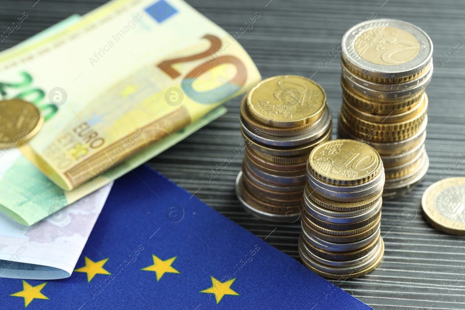 Photo of Stacks of coins, euro banknotes and European Union flag on grey textured table, closeup