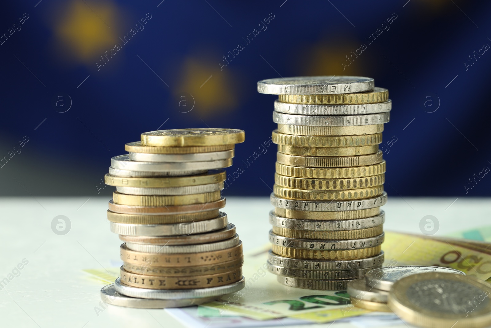 Photo of Stacks of coins and euro banknotes on white table, closeup