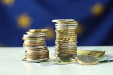 Photo of Stacks of coins and euro banknotes on white table, closeup