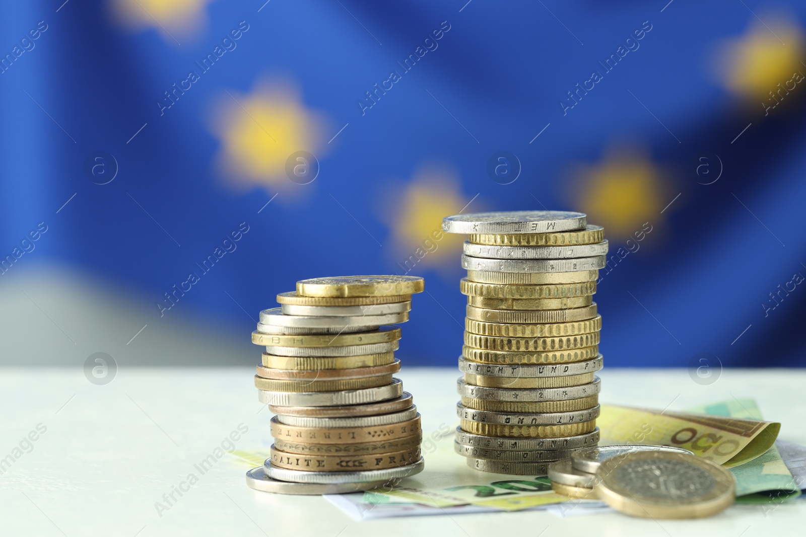 Photo of Stacks of coins and euro banknotes on white table, closeup