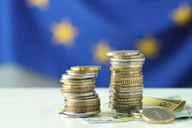 Photo of Stacks of coins and euro banknotes on white table, closeup