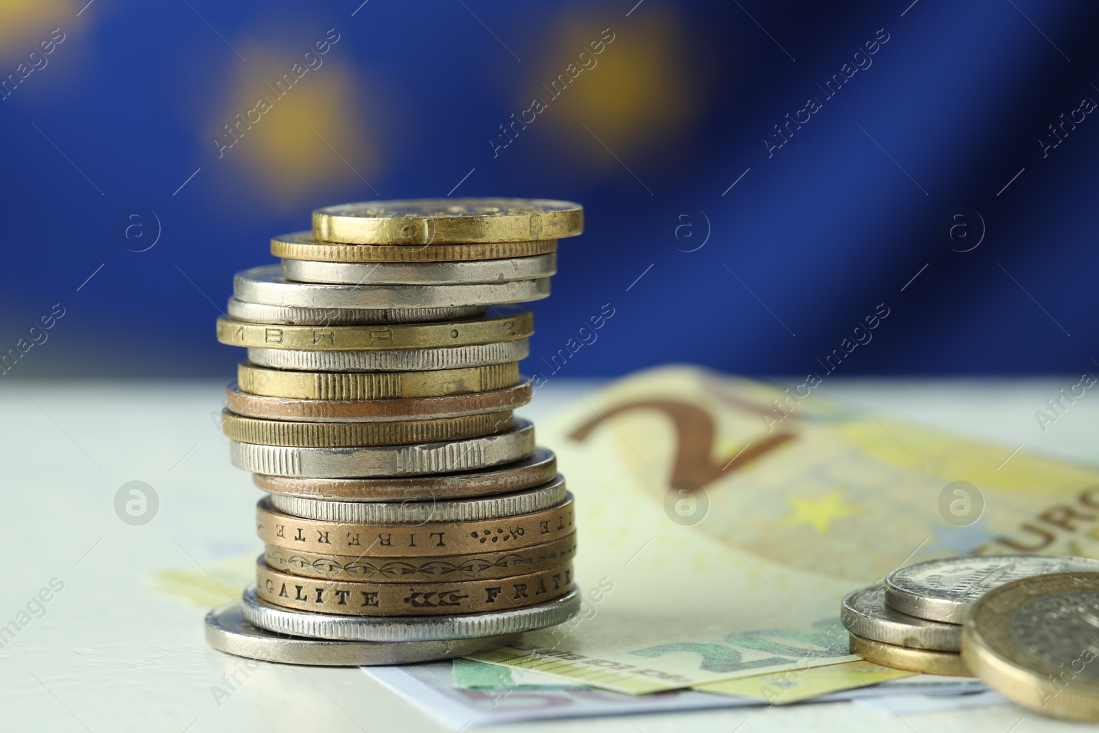 Photo of Stack of coins and euro banknotes on white table, closeup