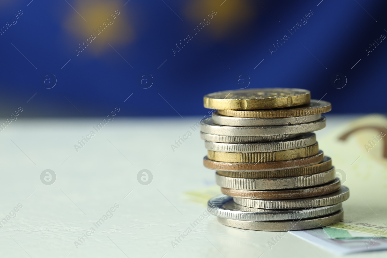 Photo of Stack of coins and euro banknotes on white table, closeup. Space for text