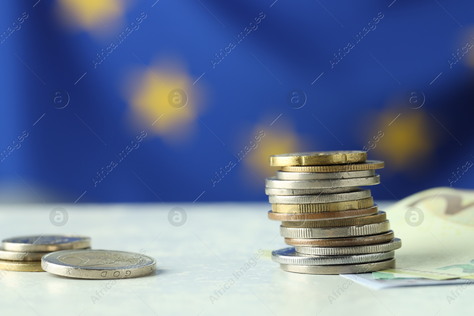 Photo of Stack of coins and euro banknotes on white table, closeup