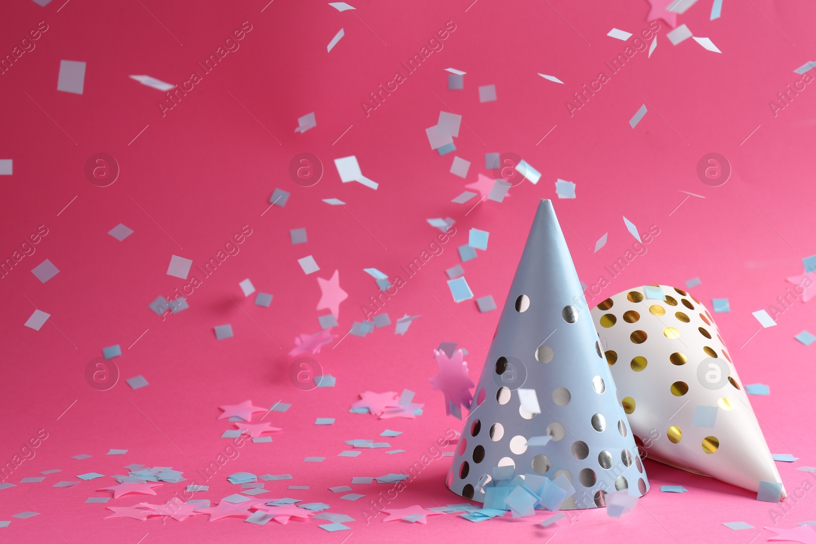 Photo of Beautiful confetti falling on party hats against pink background. Space for text