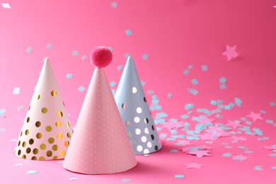 Beautiful confetti and party hats on pink background, closeup. Space for text