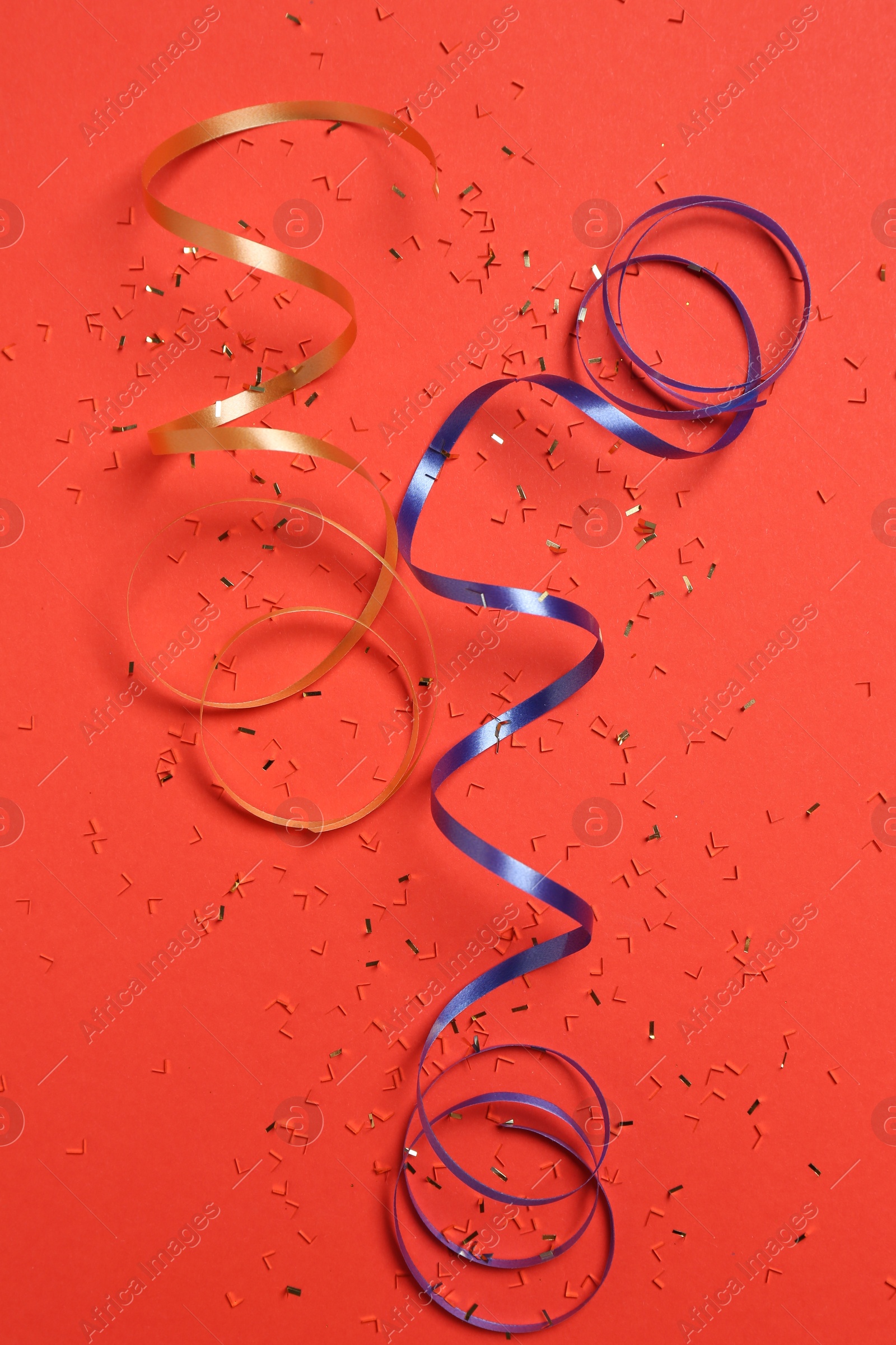 Photo of Shiny confetti and party streamers on red background, flat lay