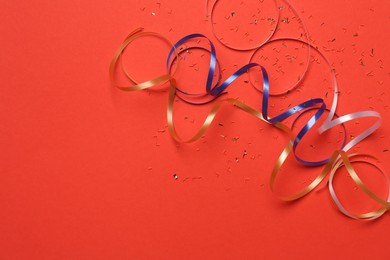 Photo of Shiny confetti and party streamers on red background, flat lay. Space for text