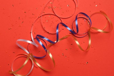 Photo of Shiny confetti and party streamers on red background, flat lay