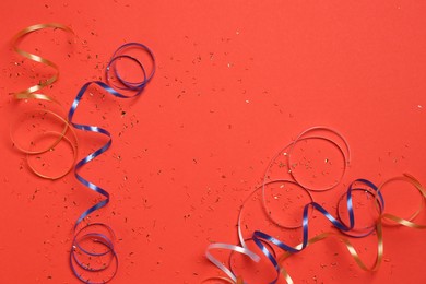 Shiny confetti and party streamers on red background, flat lay