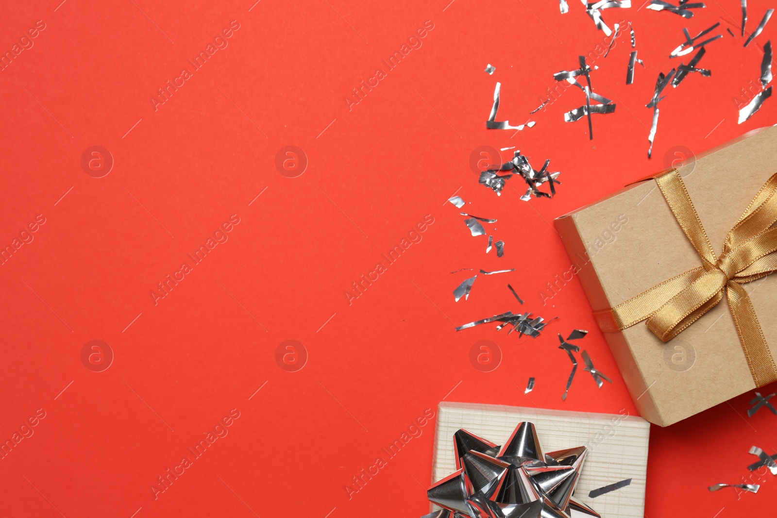 Photo of Shiny confetti and gift boxes on red background, flat lay. Space for text