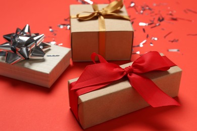 Photo of Gift boxes and shiny confetti on red background, closeup