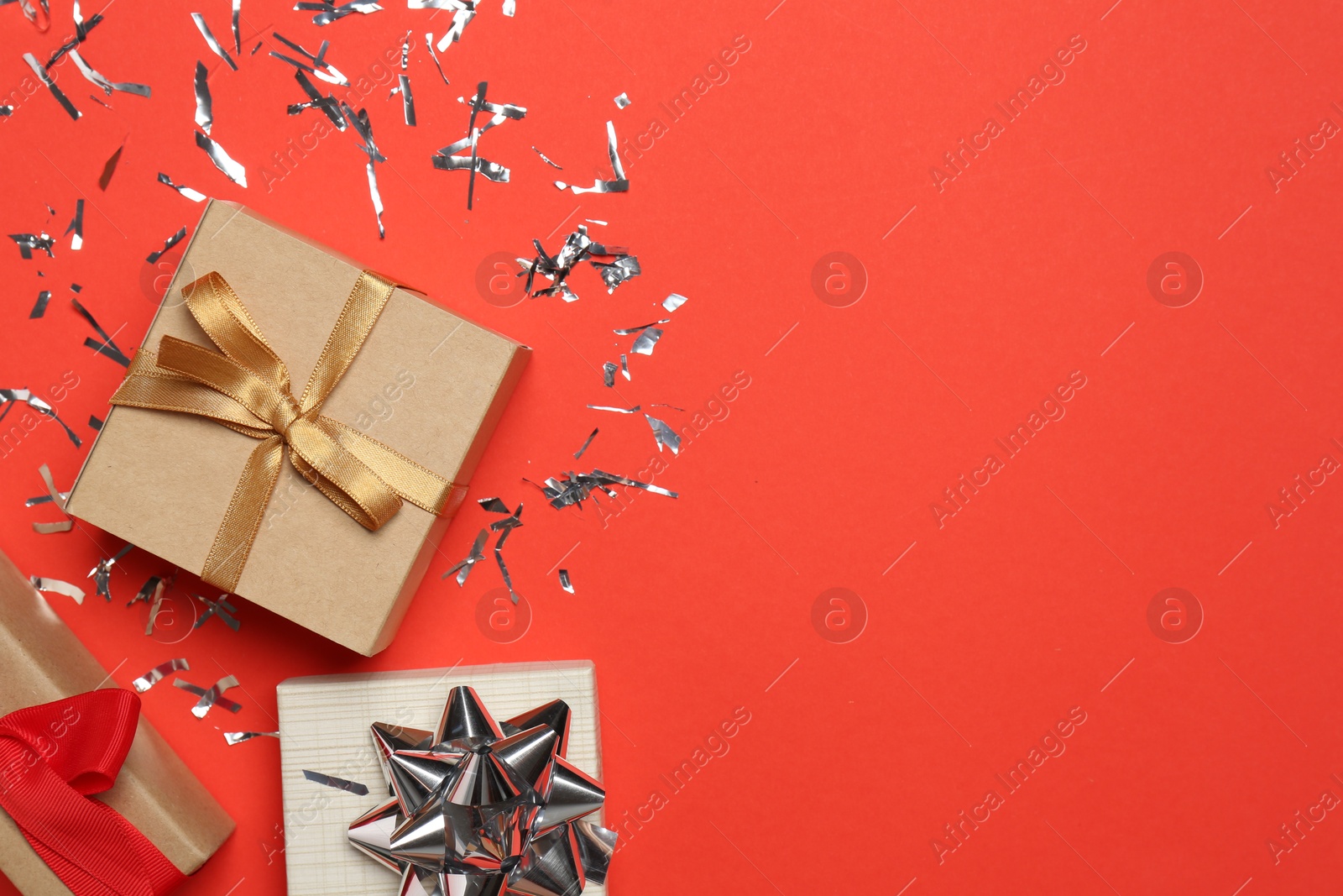 Photo of Shiny confetti and gift boxes on red background, flat lay. Space for text