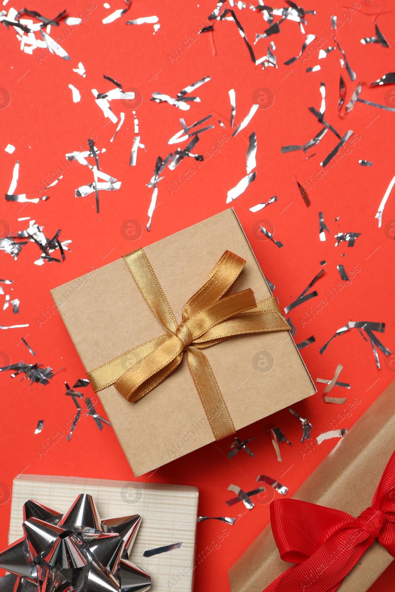 Photo of Shiny confetti and gift boxes on red background, flat lay