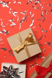 Shiny confetti and gift boxes on red background, flat lay