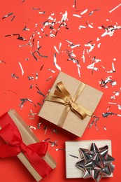 Photo of Shiny confetti and gift boxes on red background, flat lay