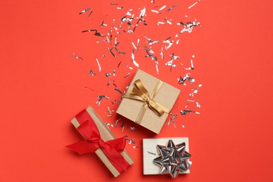 Photo of Shiny confetti and gift boxes on red background, flat lay