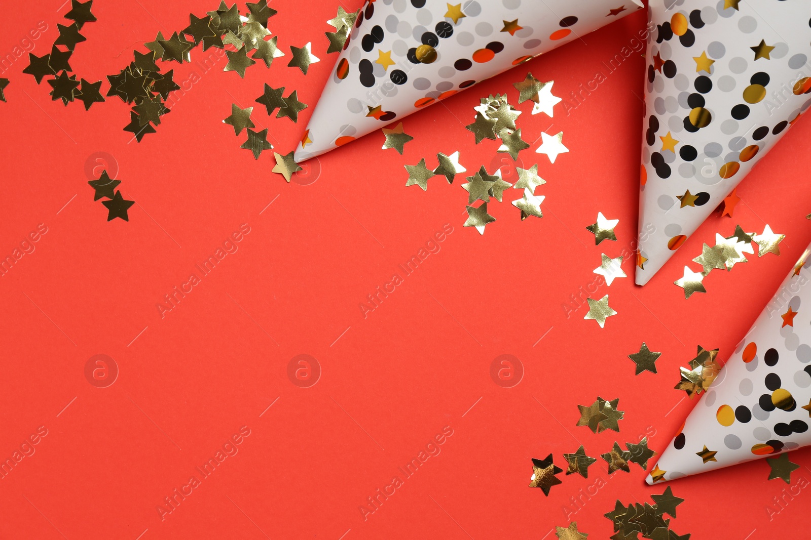 Photo of Shiny confetti and party hats on red background, flat lay. Space for text