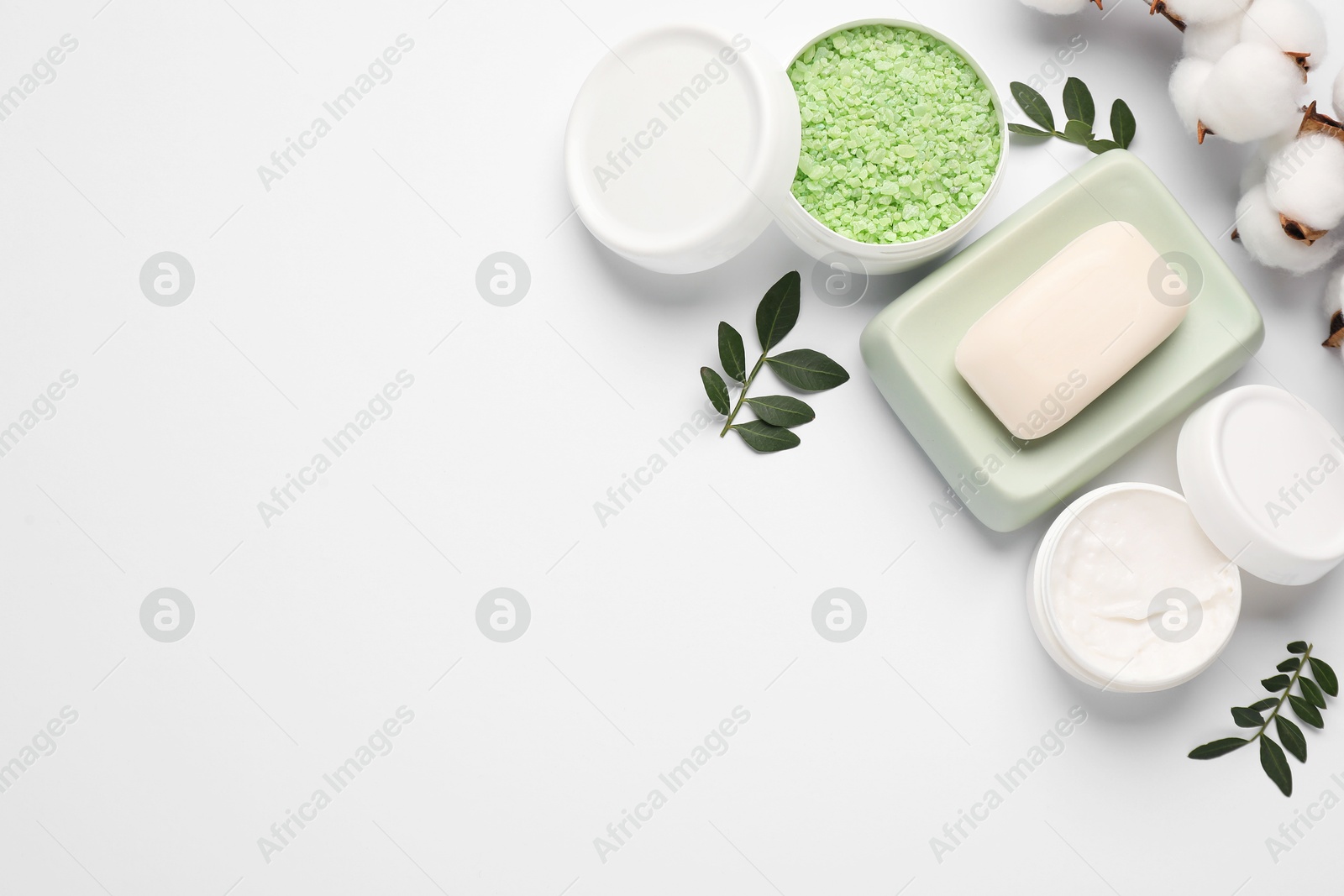 Photo of Different cosmetic products, cotton flowers and green leaves on white background, flat lay. Space for text