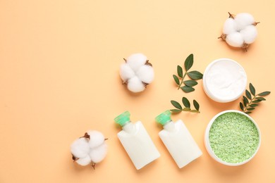 Photo of Different cosmetic products, cotton flowers and leaves on pale orange background, flat lay. Space for text