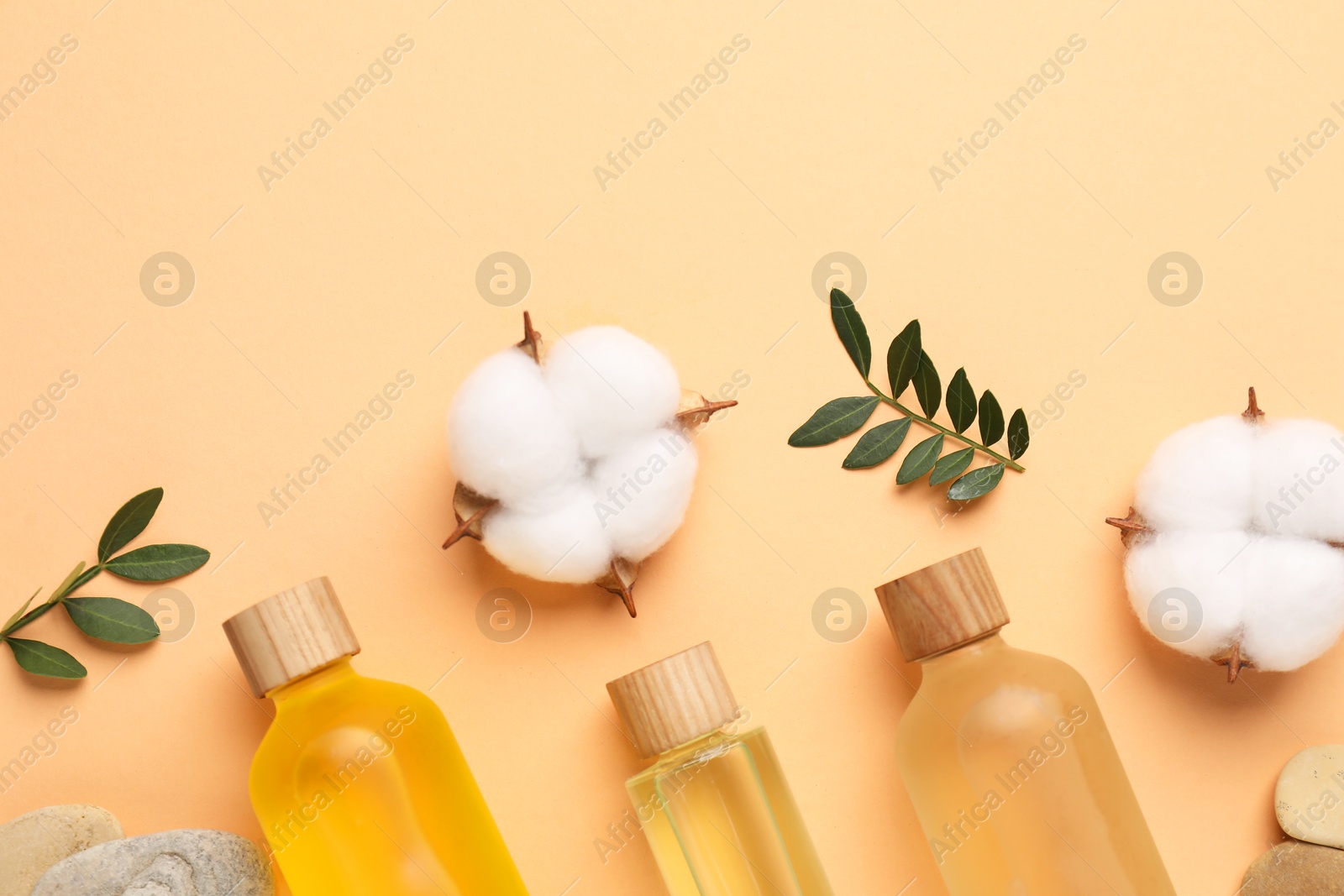 Photo of Different cosmetic products, cotton flowers and green leaves on pale orange background, flat lay