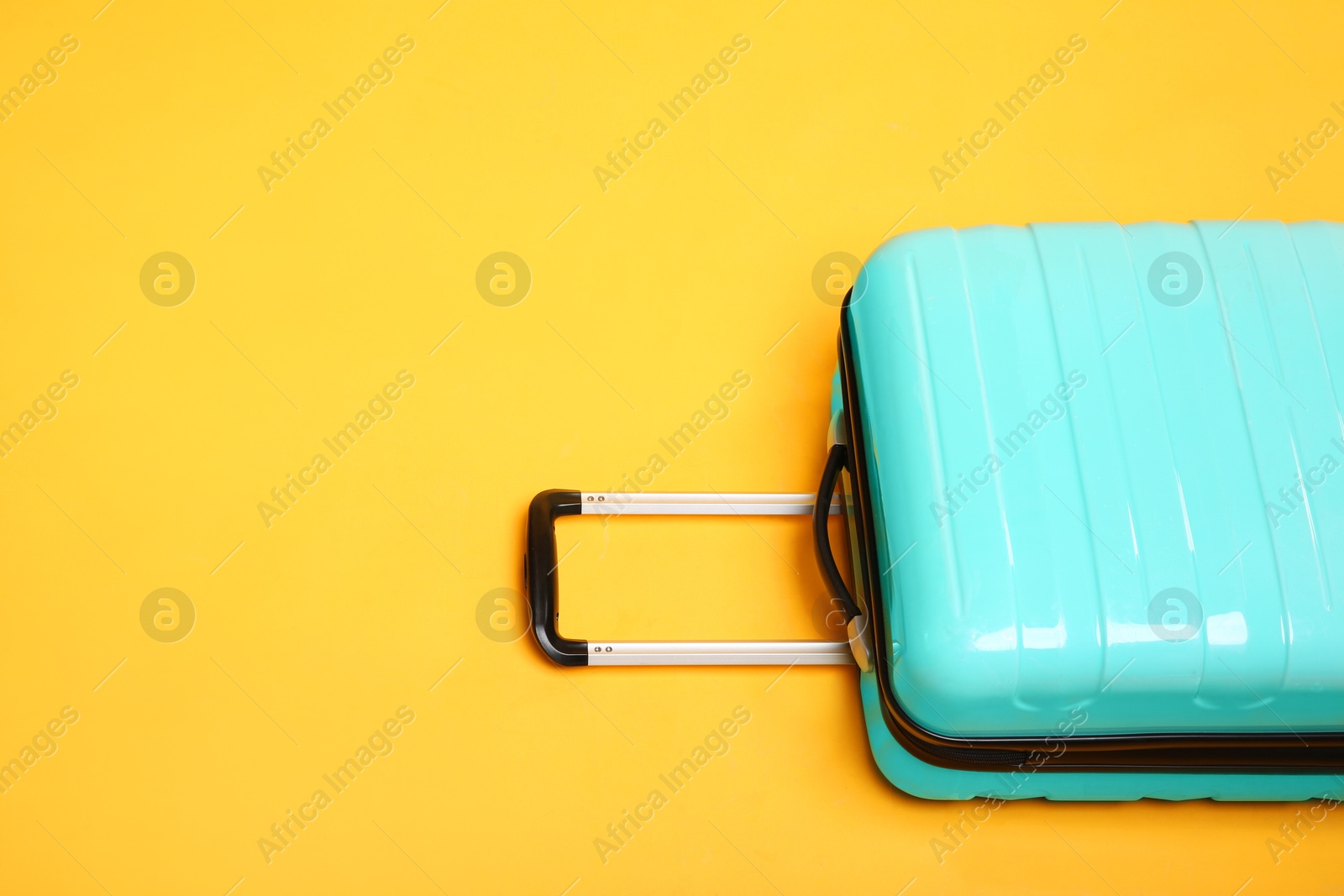 Photo of One turquoise suitcase on yellow background, space for text