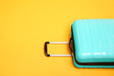 Photo of One turquoise suitcase on yellow background, space for text