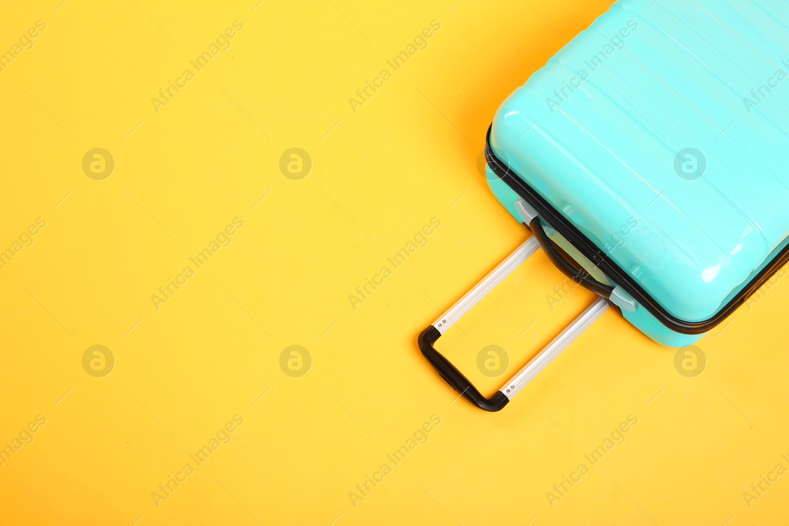 Photo of One turquoise suitcase on yellow background, above view. Space for text