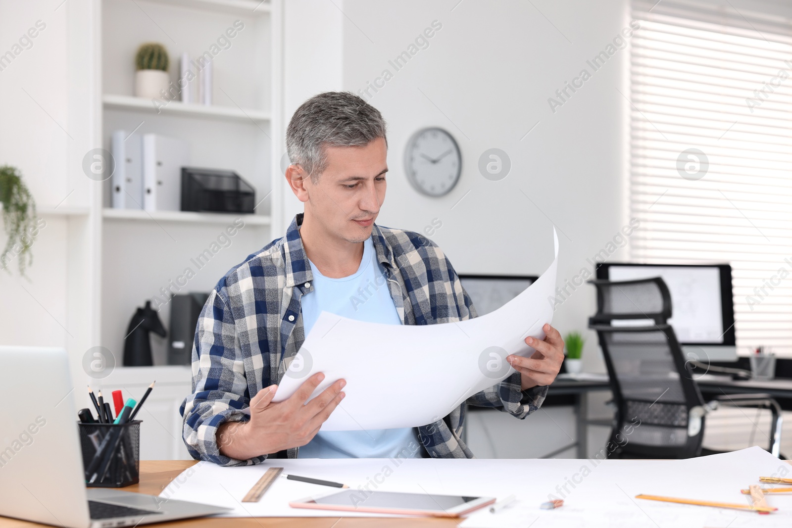 Photo of Architect checking engineering drawing at table in office