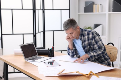 Photo of Architect making engineering drawing at wooden table in office