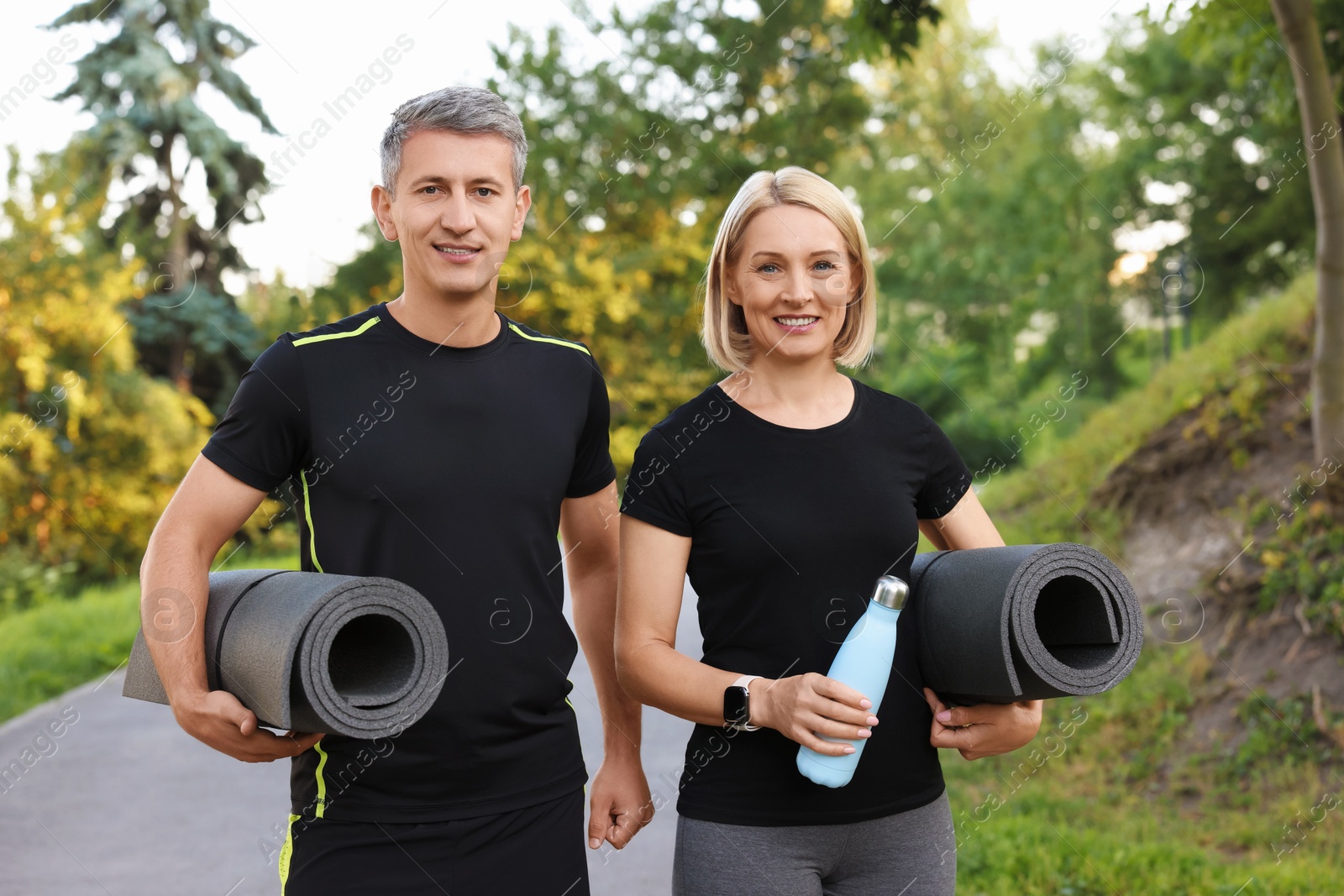 Photo of Happy couple with bottle of water and fitness mats in park