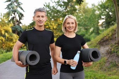 Photo of Happy couple with bottle of water and fitness mats in park