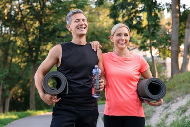 Photo of Happy couple with bottle of water and fitness mats in park