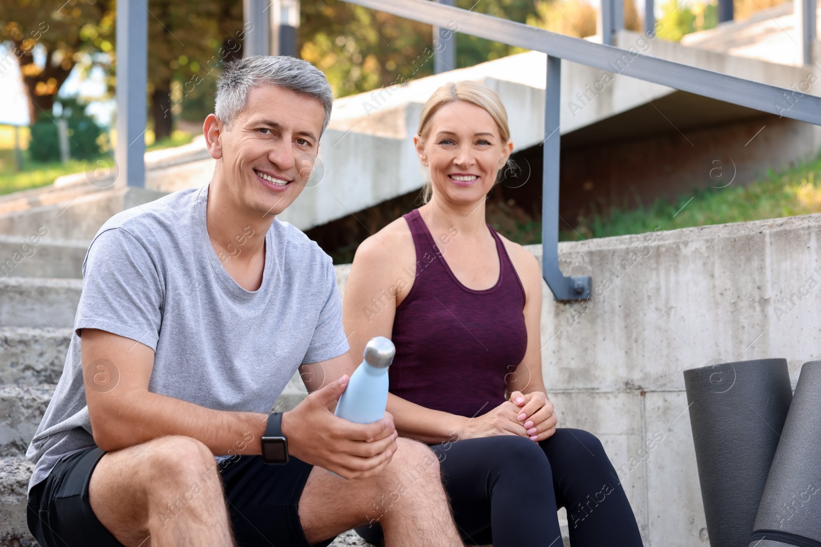 Photo of Smiling couple with bottle of water on steps outdoors